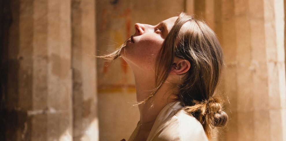 A woman in a beige coat looks up inside ancient Egyptian temple ruins.