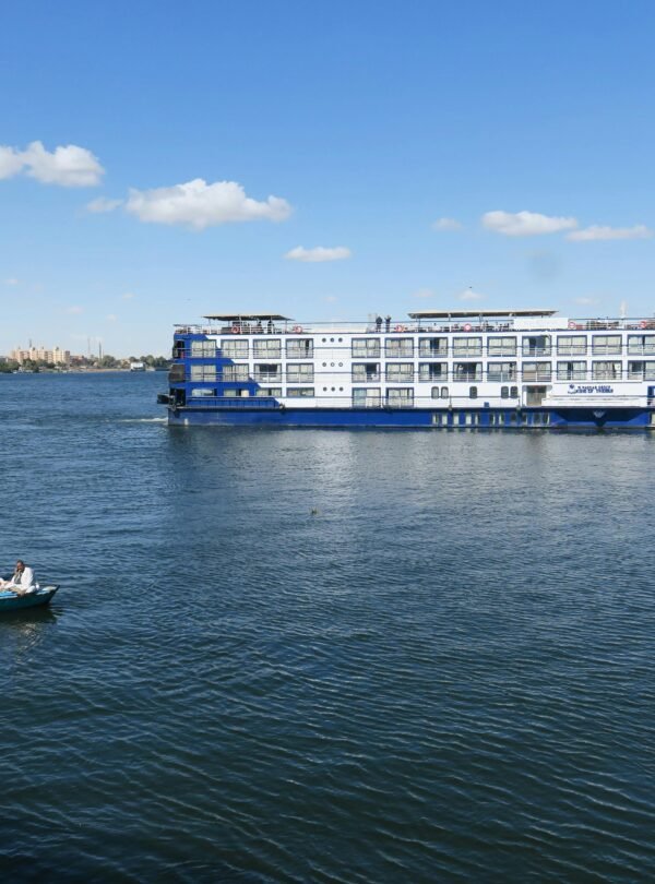 A ferry boat and rowboat on the Nile River under a clear blue sky in Luxor, Egypt.