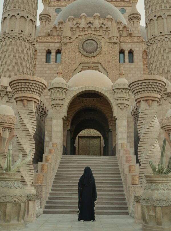 A woman in black robe stands before an intricate mosque, highlighting traditional architecture.