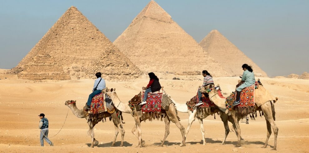 Tourists riding camels near the Great Pyramids of Giza, Egypt under clear skies.